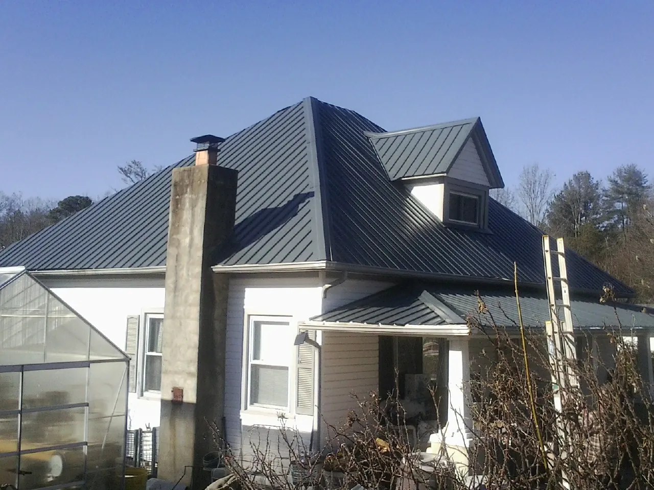 Dark blue standing seam metal roof on a white farmhouse with dormer — Slate & Tile Roof Repair by Roofing Brothers in Pleasant Grove