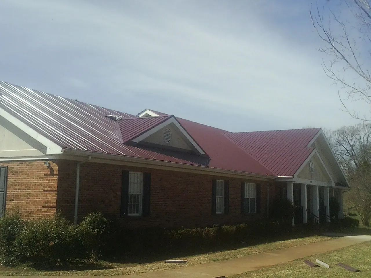 Red metal roof with gabled entries on a long brick building, from a Hail Damage Roof Repair job in Pleasant Grove