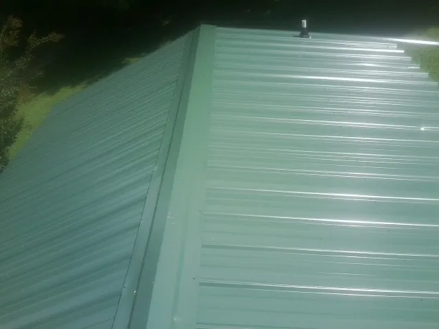 New green metal panels meeting at the ridge of a roof — Flat Roof Repair work by our crew in Pleasant Grove