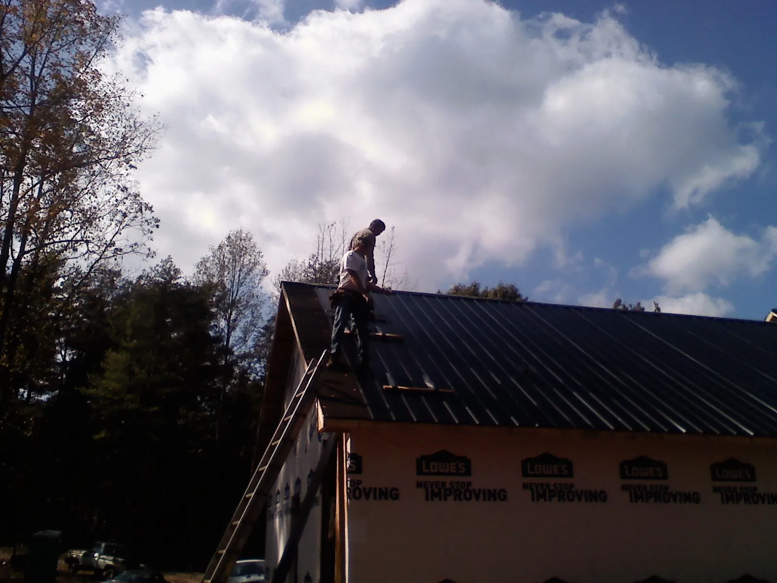Roofer fastening dark metal panels high against a cloudy sky, from a Roof Inspection job in Pleasant Grove