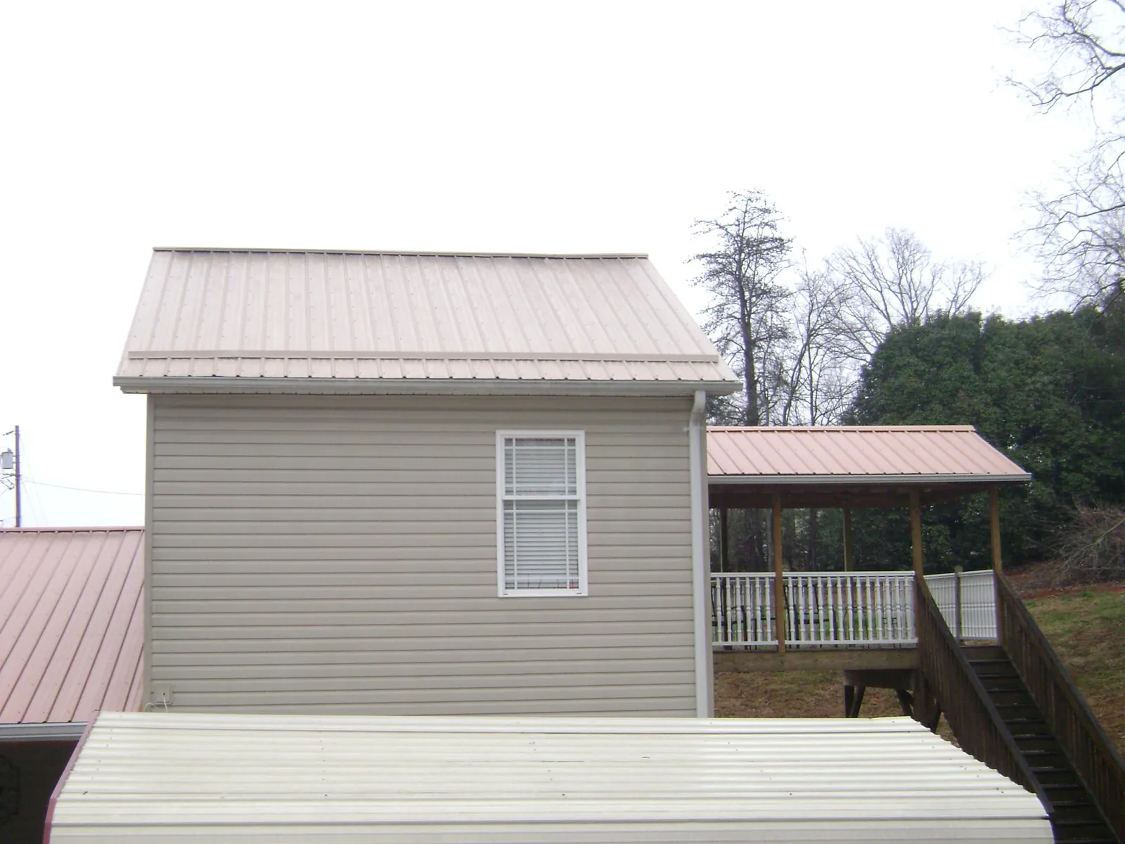 Tan metal roofs on a two story addition and attached porch, from a Roof Replacement job in Pleasant Grove